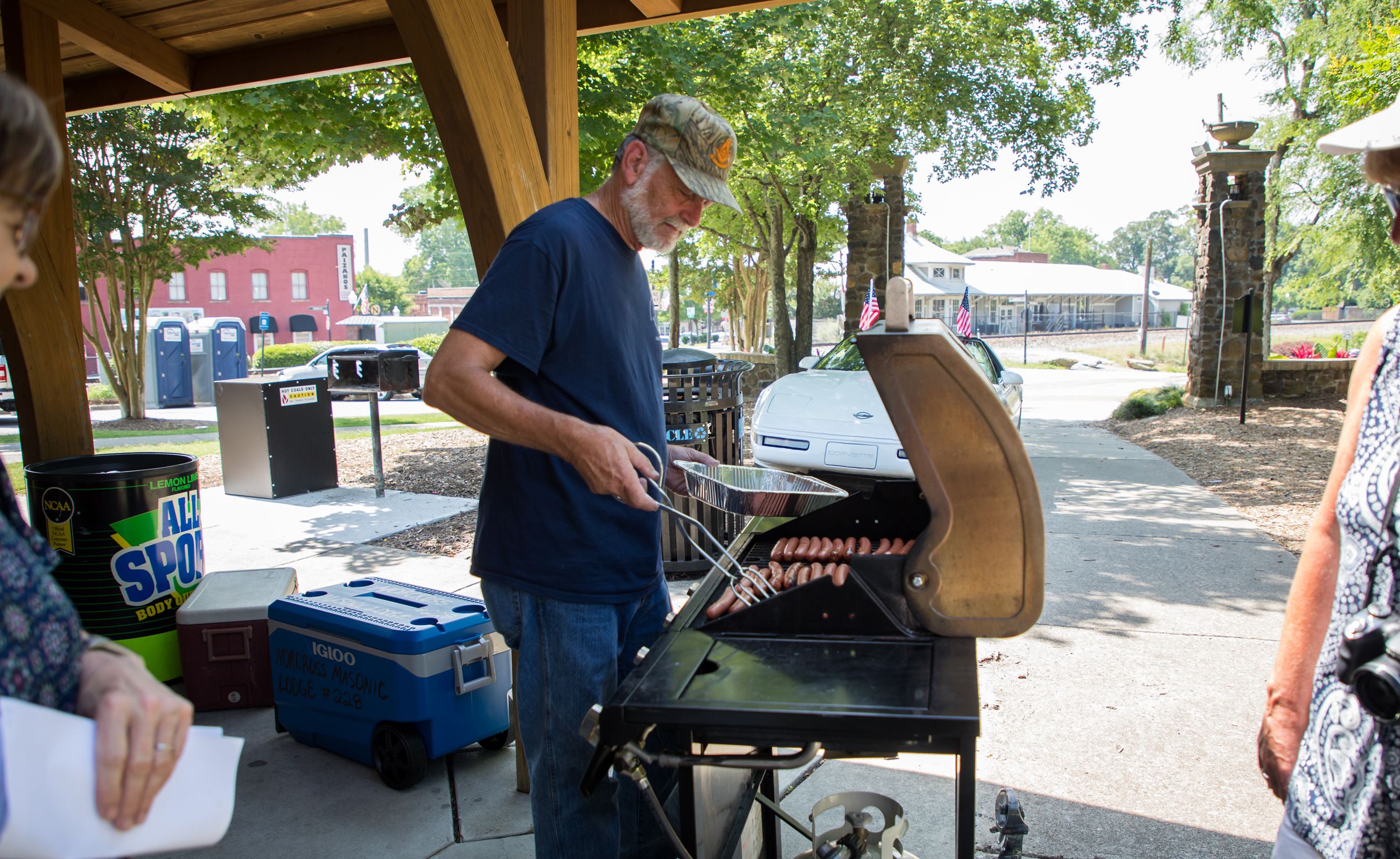 man grills hot dogs under picnic pavilion