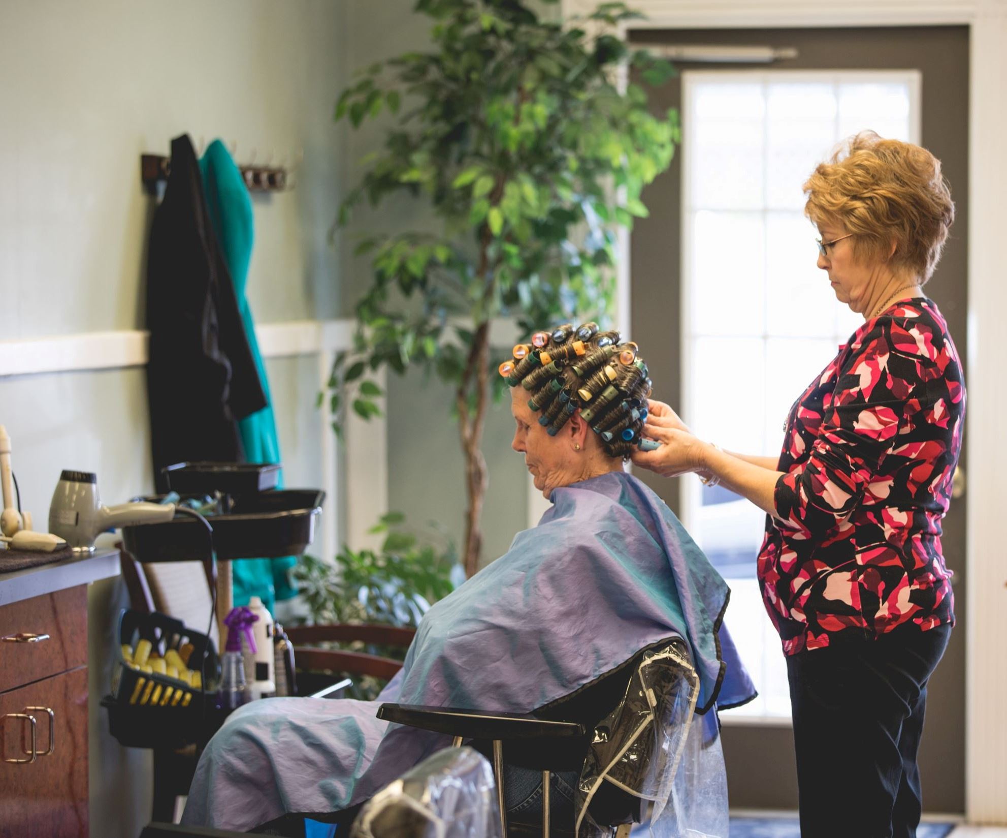 Women sitting in chair as stylist puts curlers in her hair